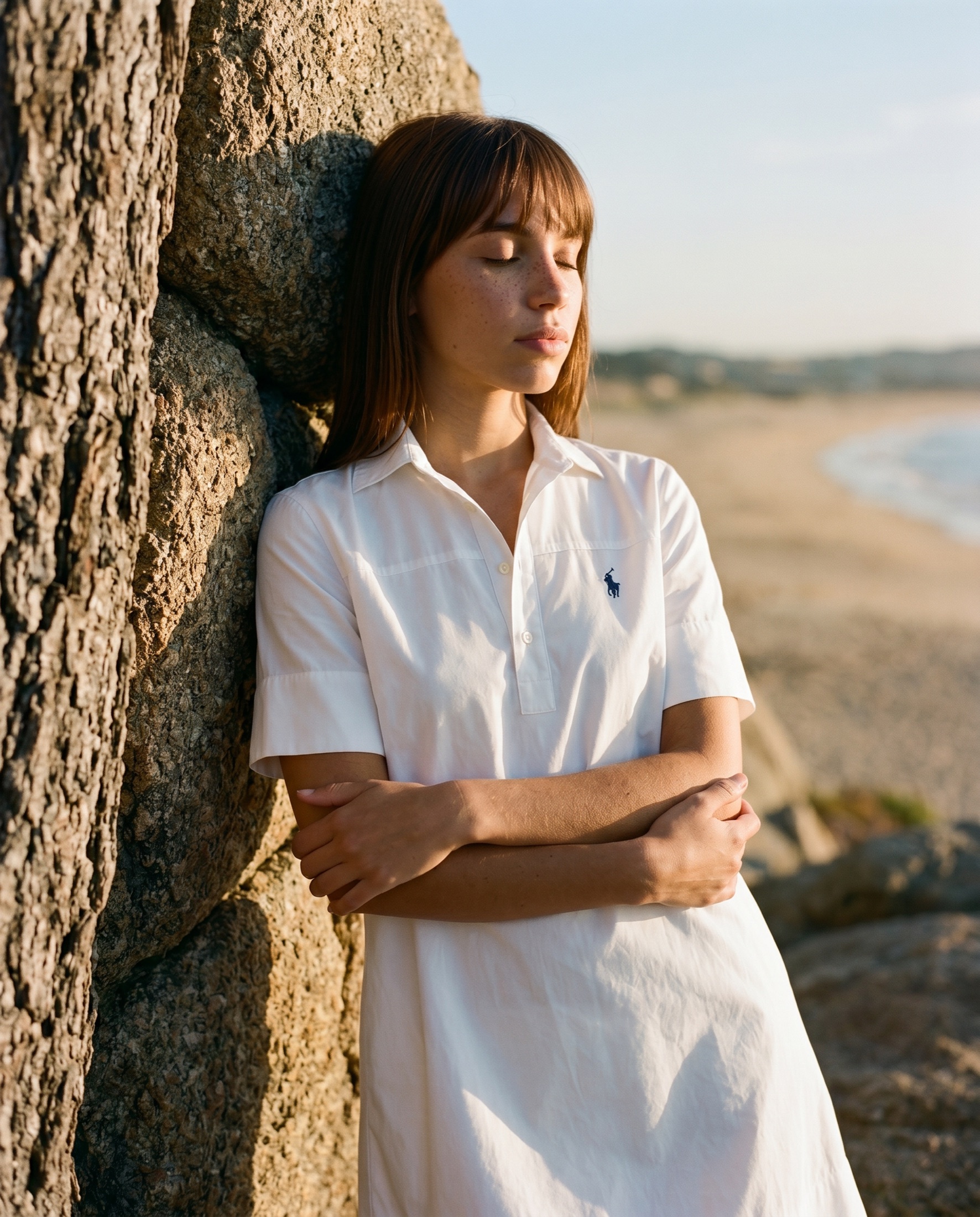 Ralph Lauren lifestyle campaign — white cotton dress leaning against a sea-cliff rock at golden hour